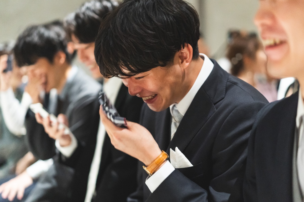 結婚式当日、スマートフォンを見て笑う参列者の様子